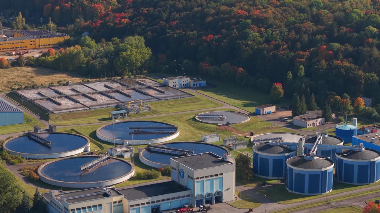 Aerial view of a modern wastewater treatment plant in Kaunas, Lithuania, featuring circular sedimentation tanks and advanced infrastructure set against a colorful autumn forest backdrop