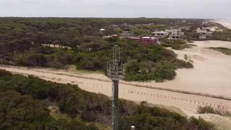 aerial orbit shot of network antenna at beach and forest of mar de las pampas sending signal waves to city,argentina