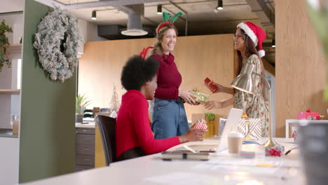 felices y diversas colegas creativas dando regalos de navidad en la oficina, en cámara lenta