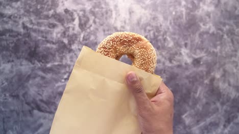 mano sosteniendo un bagel de sésamo en una bolsa de papel