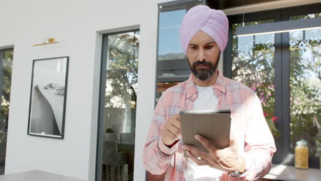 using tablet, man in turban standing in modern home, concentrating on screen