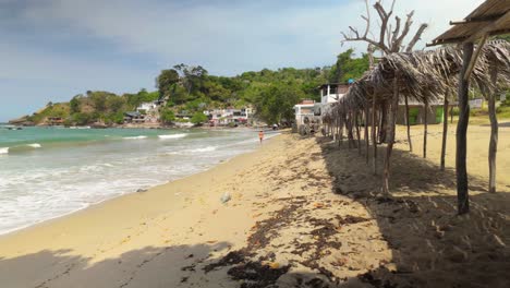 A beach scene with palm patterns and a woman’s stroller in the foreground, set against crashing waves and turquoise waters of the Caribbean Sea along the wide shoreline of Urama Beach, Venezuela.