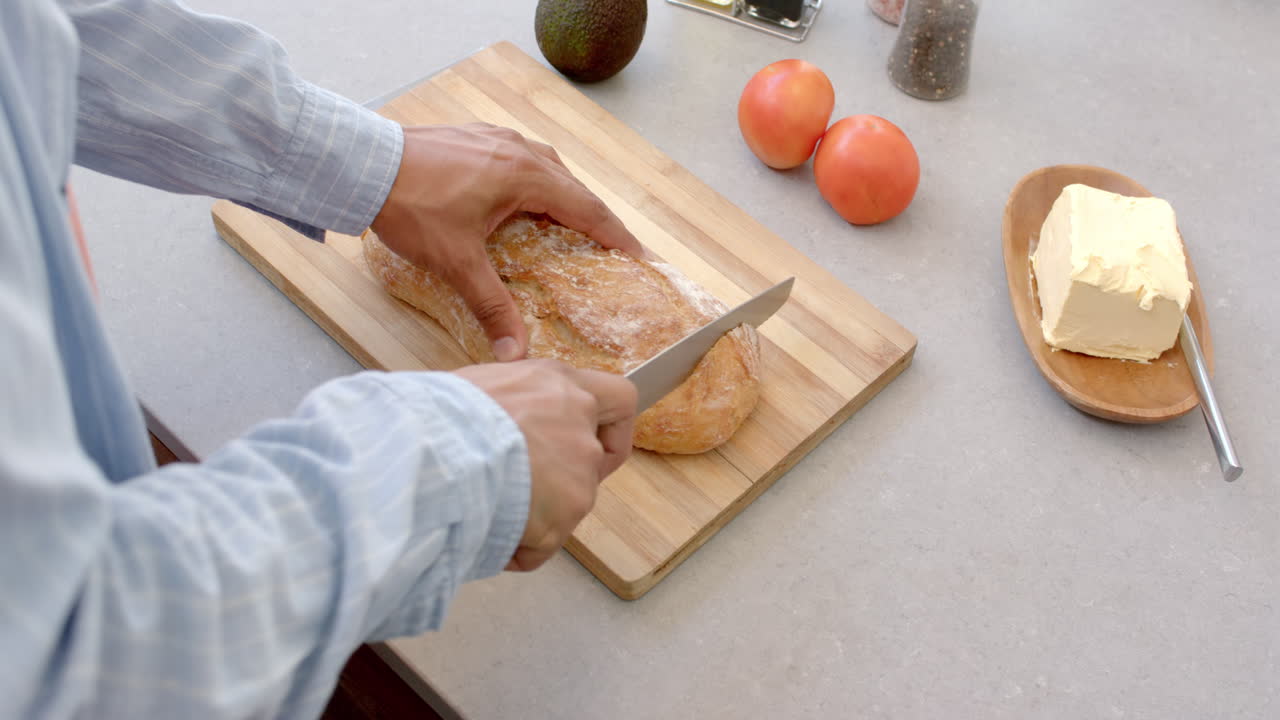 Slicing bread on cutting board, man preparing meal with tomatoes and avocado