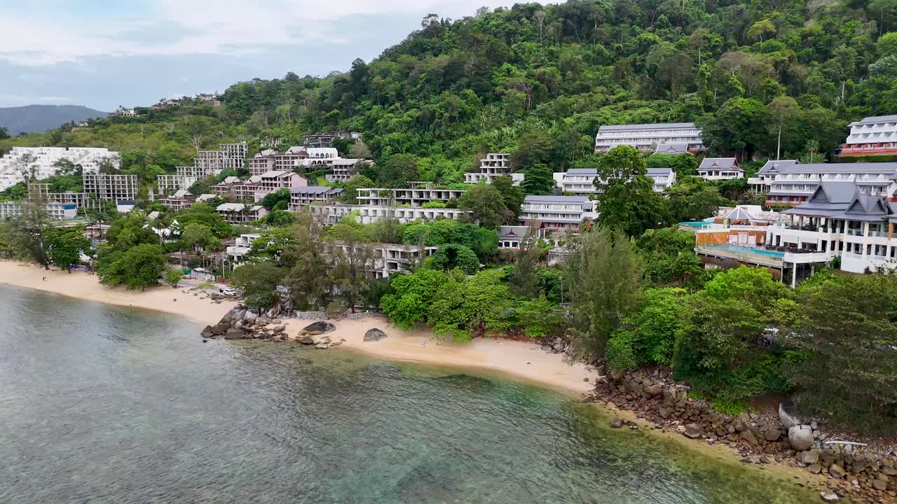 공중 촬영은 푸켓의 조용한 해안선을 따라 울창한 초록색과 해안 휴양지를 포착하여 활기찬 풍경과 조용한 물을 보여줍니다.