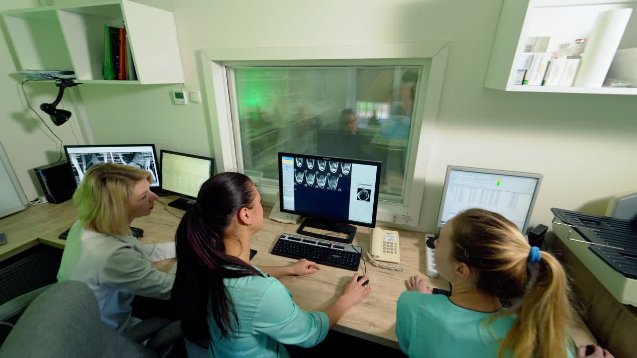 Medical workers in control room in clinic. Doctors sitting at workplace and looking at the screen of computer with a patient's x-ray shot.
