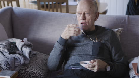 elderly man taking medication and drinking milk on couch