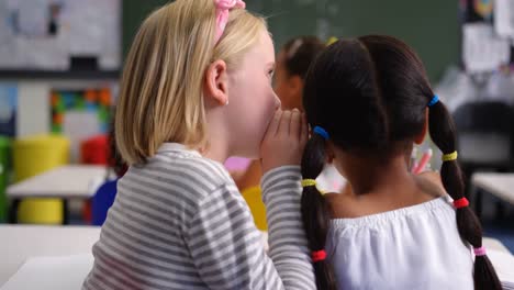 rear view of mixed-race schoolgirl whispering in her classmates ear at classroom 4k