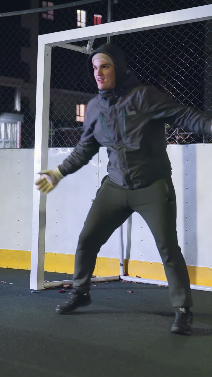 portero practicando habilidades defensivas cerca del poste de la portería durante la sesión de entrenamiento nocturna en la cancha deportiva al aire libre, la escena captura la preparación atlética con un fondo urbano iluminado