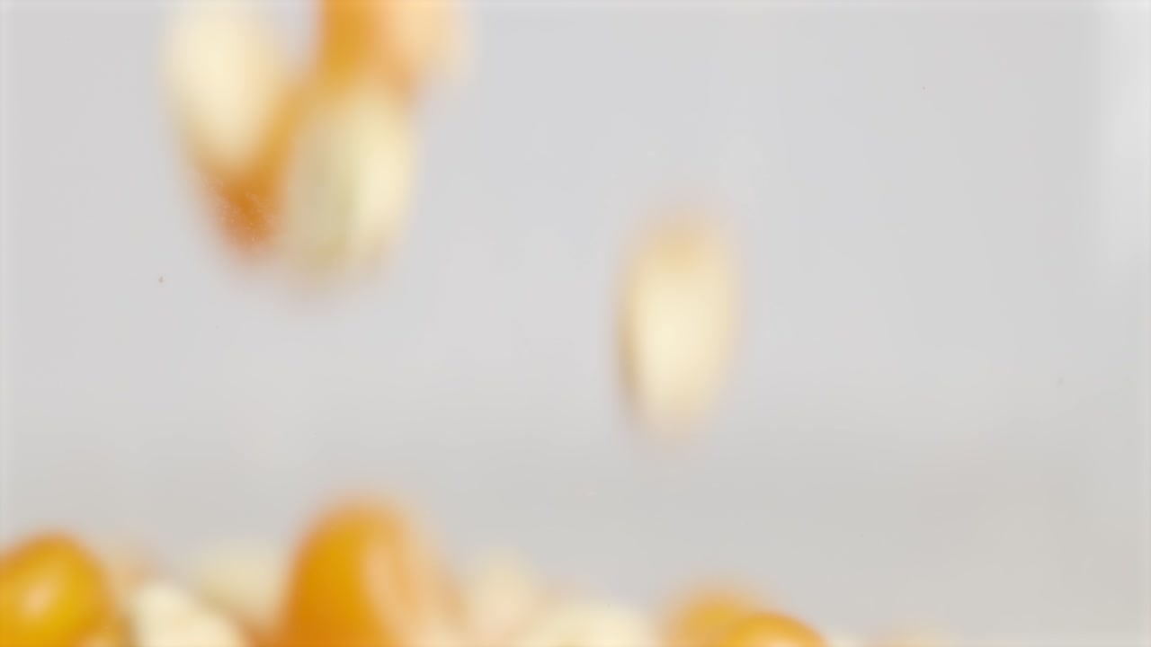 Macro video captures popcorn kernels falling in slow motion against a neutral background, highlighting texture and movement