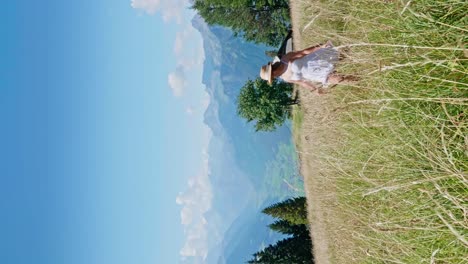 Vertical-shot-of-happy-woman-doing-frisk-in-grass-field-during-sunny-day-in-alps