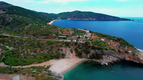 Una-Vista-De-Pájaro-De-Una-Playa-Aislada-Con-Aguas-Turquesas,-Casas-En-Los-Acantilados-Y-Exuberante-Vegetación,-Isla-De-Thassos,-Grecia