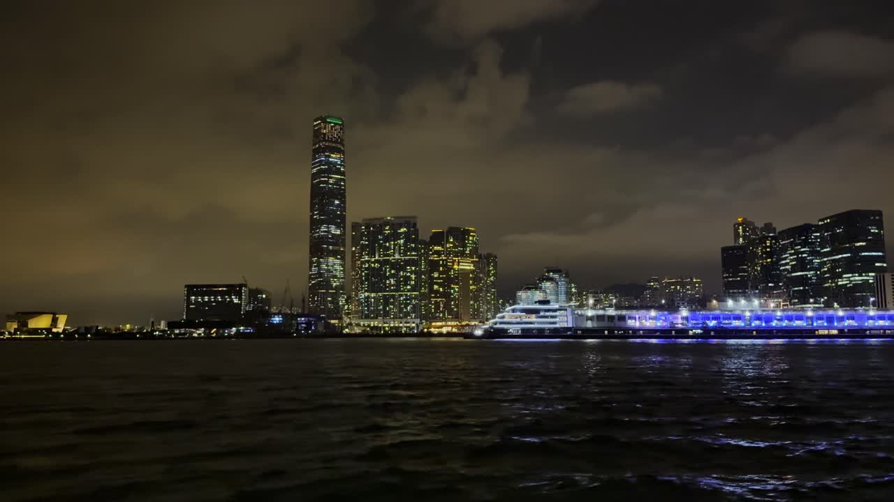 Footage of Hong Kong harbour at night, showcasing illuminated skyscrapers, glowing waterfront, and reflections on the water, capturing the vibrant urban energy and iconic city skyline after dark