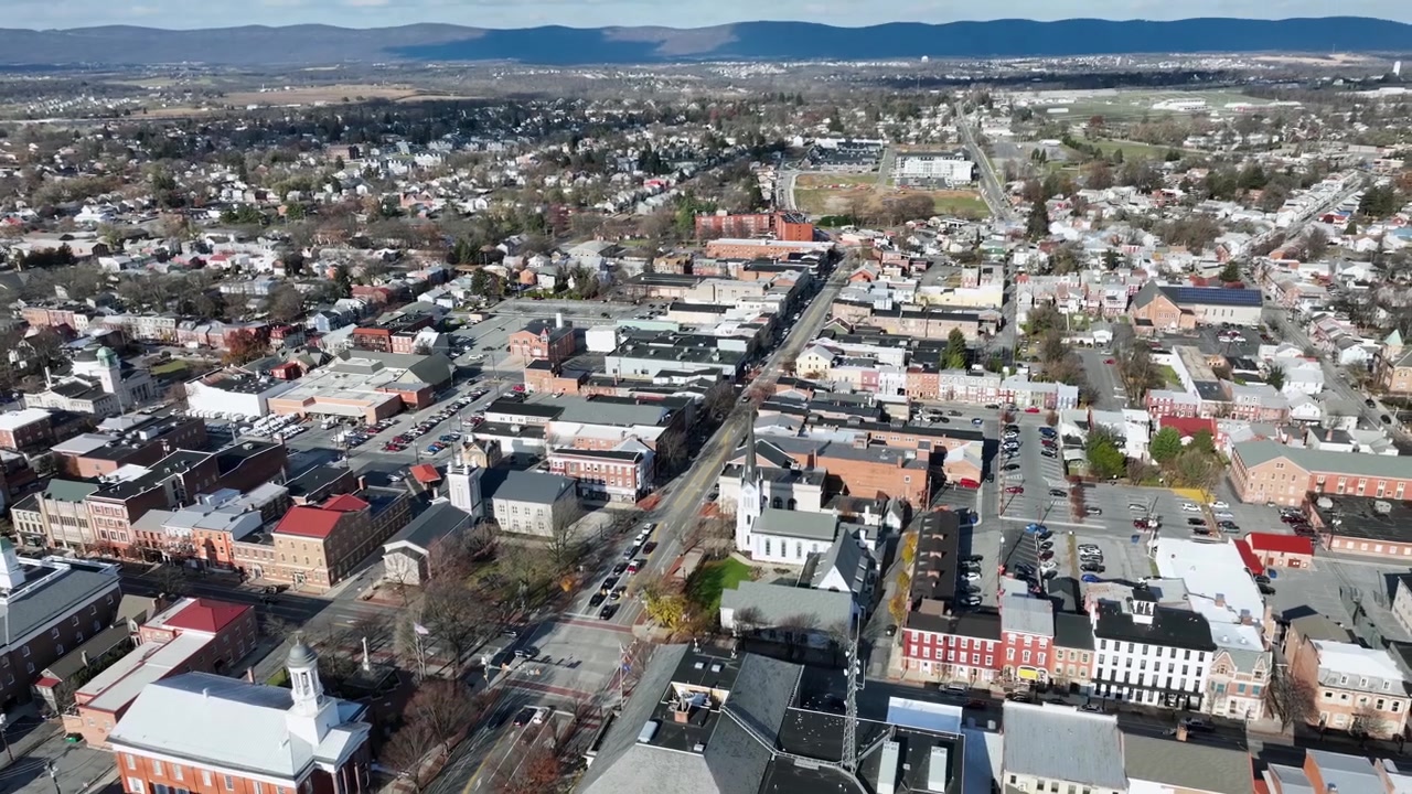 Small American town during sunlight in fall season. Carlisle town from above, Pennsylvania, USA. Aerial tilt up wide shot. Driving cars on main junction. Sunny autumnal day in November.