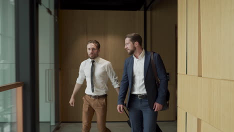 two young businessmen walking through the corridors of the airport carrying a trolley and a bag during a business trip