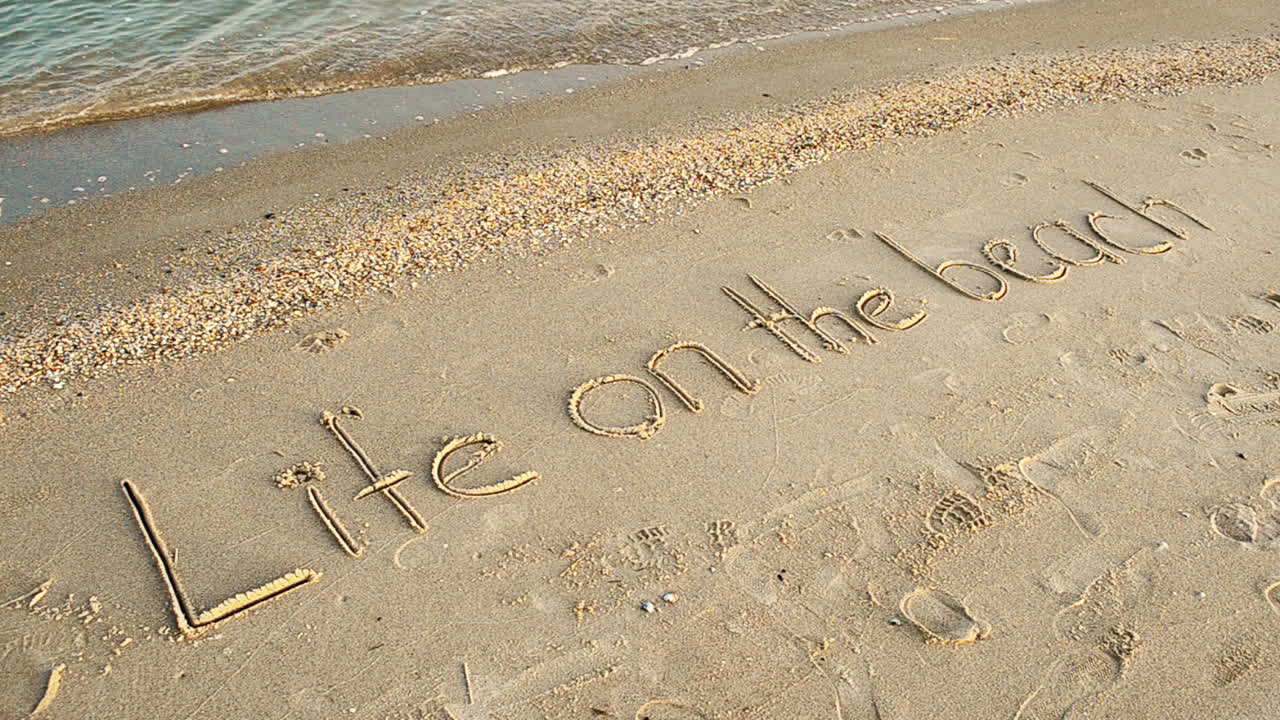 Optagelse på stranden. Livet på stranden-koncept – inskription i strandsand med en kommende bølge.