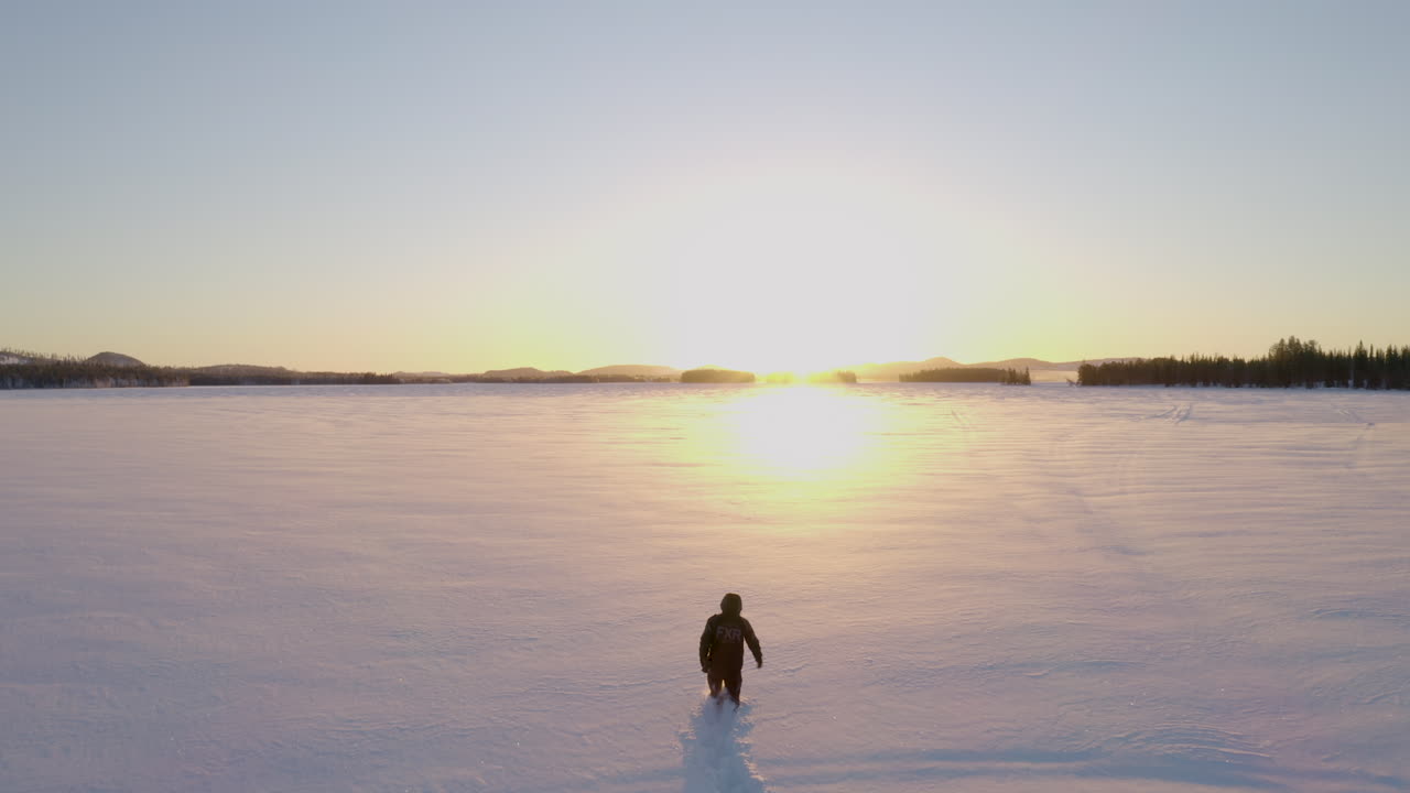 빛나는 황금빛 일출, 스웨덴을 향해 깊은 눈이 얼어붙은 호수를 걷는 남성