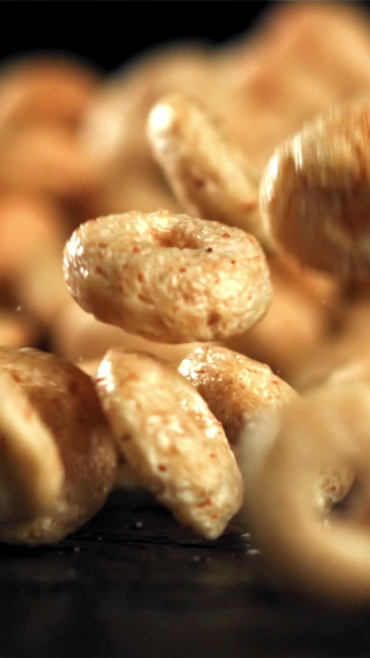 Anelli di cereali dorati che cadono al rallentatore su una superficie scura.
