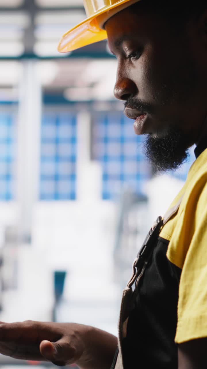 Vertical Video Black technician in solar panel facility reviews photovoltaic system performance