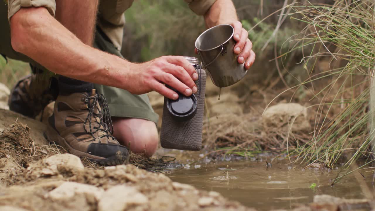 sobreviviente caucásico masculino recogiendo agua de un arroyo y vertiendo en una botella de filtro para beber