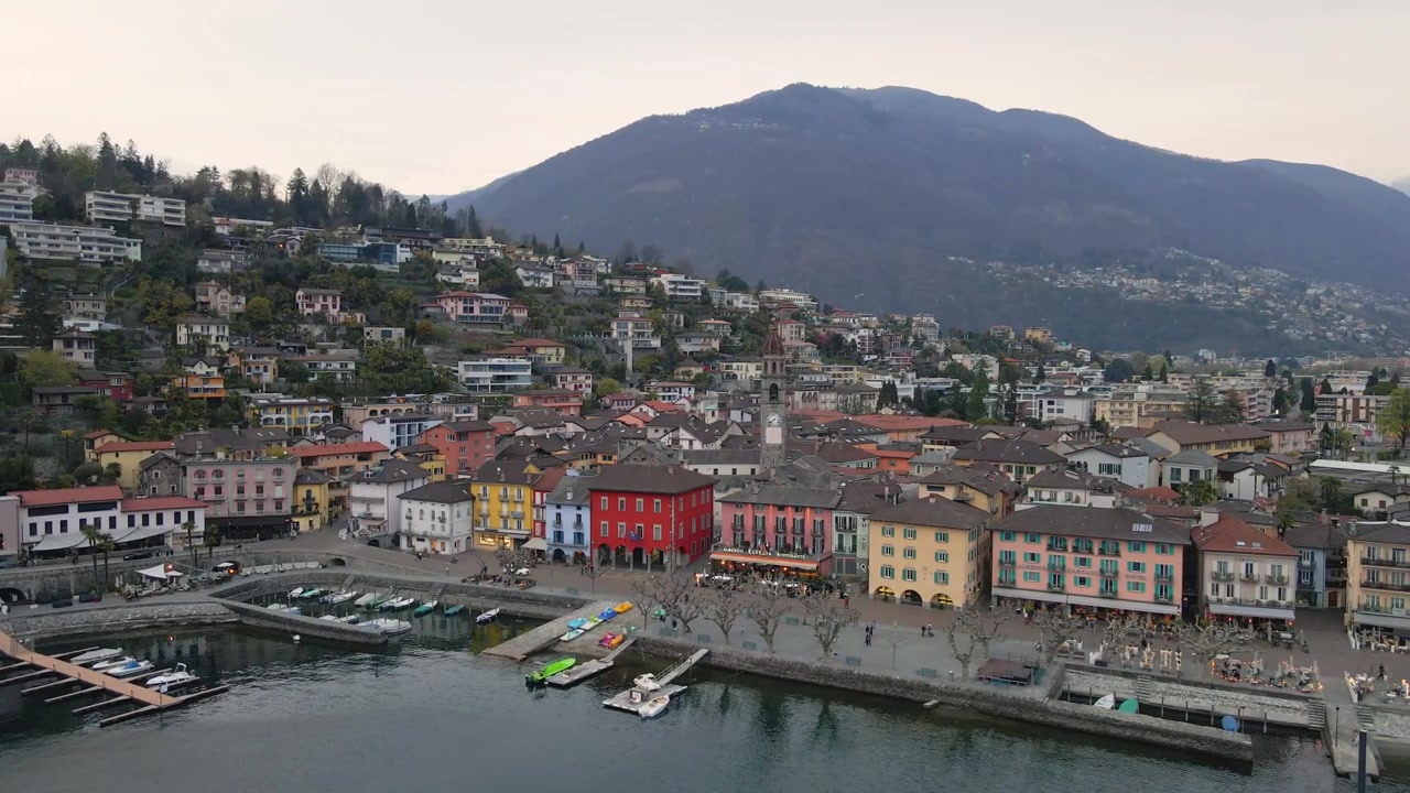 Case colorate costeggiano il lungolago di Ascona, Svizzera, incastonate sullo sfondo delle Alpi e del Lago Maggiore, Canton Ticino, Svizzera, ripresa aerea con drone in orbita