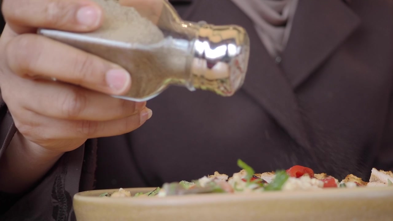 Person Seasoning a Fresh Salad with Black Pepper