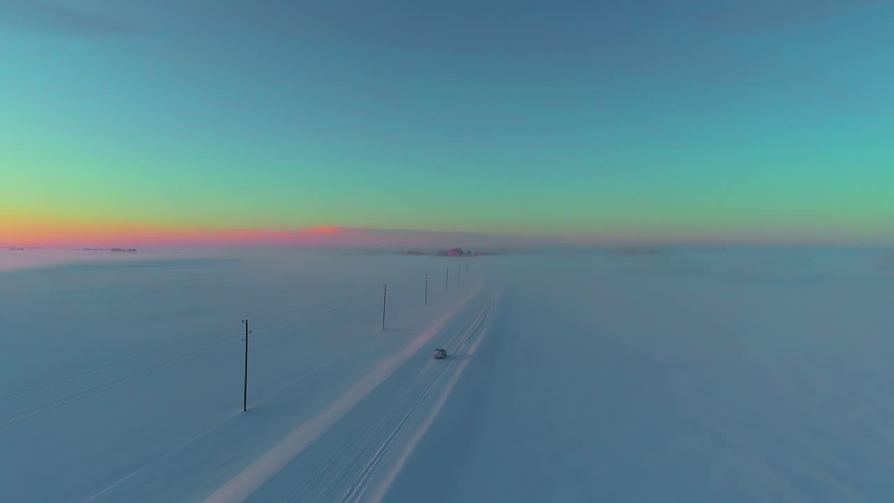 황혼에 눈 덮인 시골 길을 운전하는 자동차 - 공중 추적