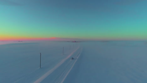 car driving down a snow-covered countryside road at twilight - aerial follow