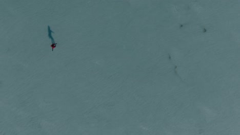 aerial shot girl ice skating on a frozen lake wearing a red shawl, on a clear sunny day, serene moments