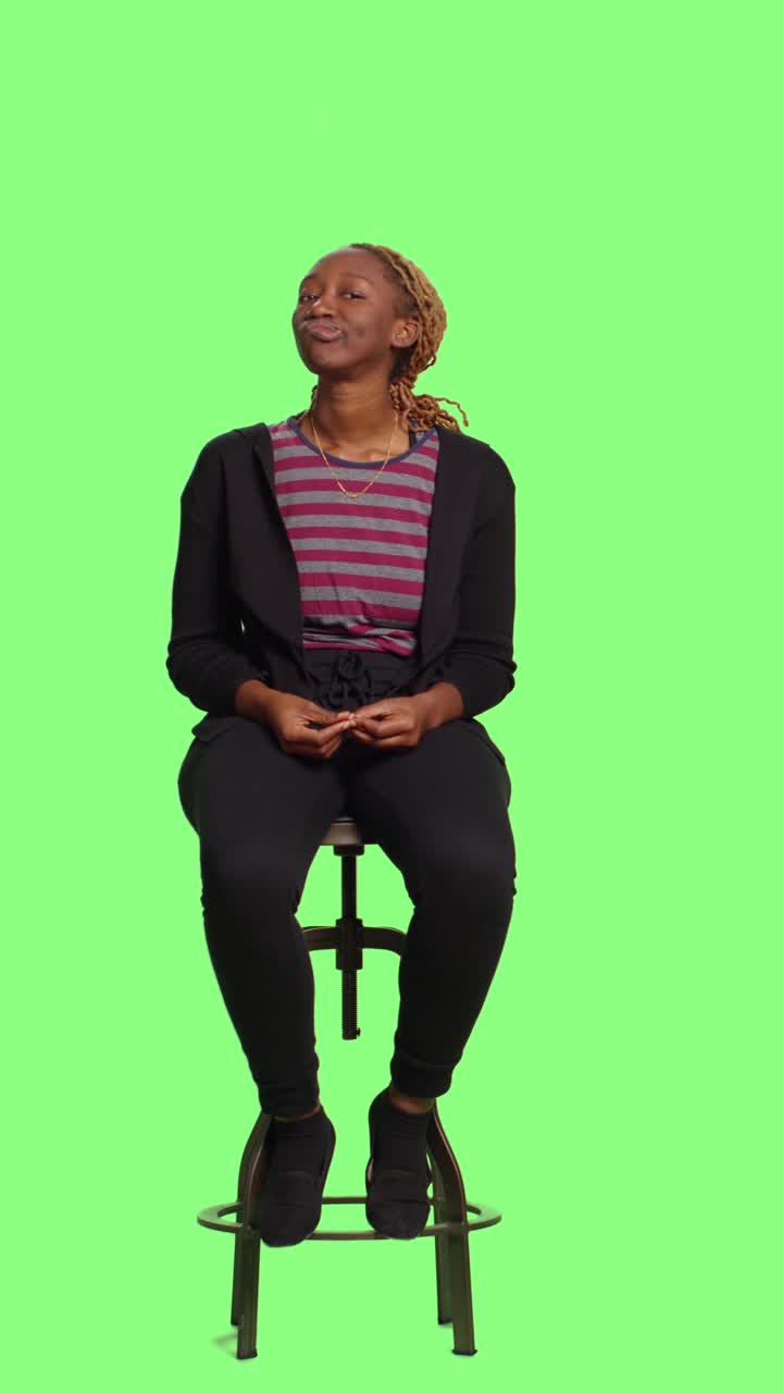 Vertical video: Modern young adult on chair waiting on green screen backdrop
