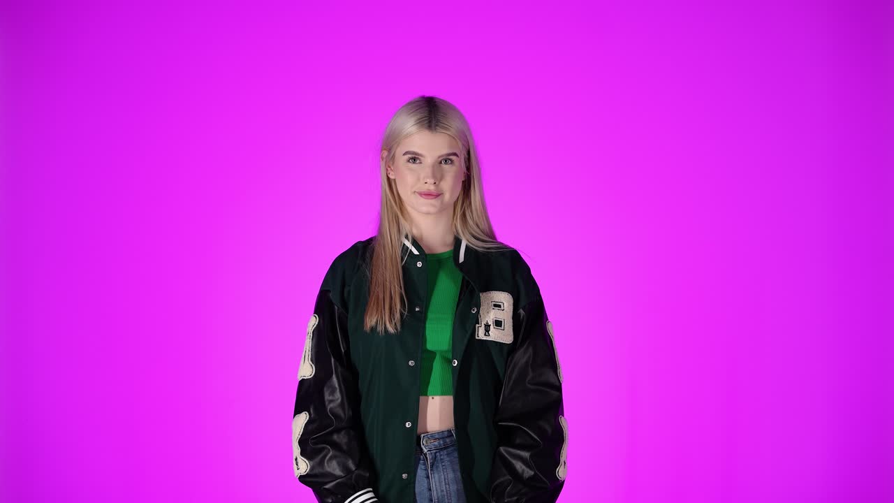 Giovane donna bionda che saluta con la mano, su sfondo viola, scatto in studio.