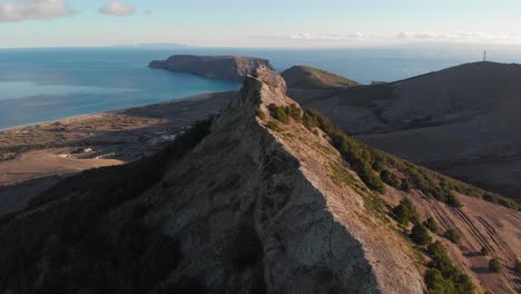 Backward-flight-directly-above-and-along-Ana-Ferreira-peak-ridge-Porto-Santo-island-with-scenic-view-of-blue-ocean-sea-water-on-sunny-day,-archipelago-of-Madeira,-Portugal,-overhead-aerial-pull-back