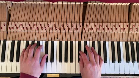 overhead view of a piano and two white hands playing the notes