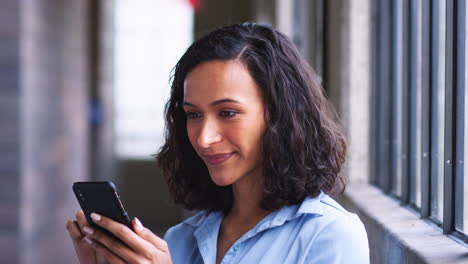 Lächelnde-Junge-Geschäftsfrau-Mit-Gemischter-Abstammung,-Die-Auf-Ihr-Smartphone-Schaut