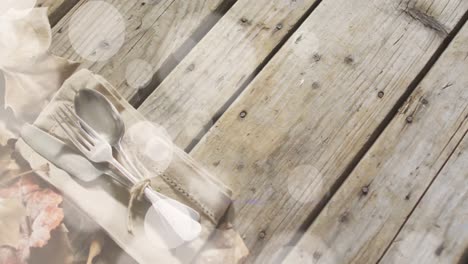 animation of light spots over cutlery and leaves on wooden background