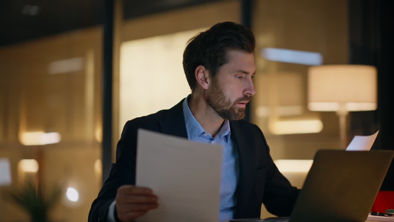 Serious professional examining documents at night office workspace closeup
