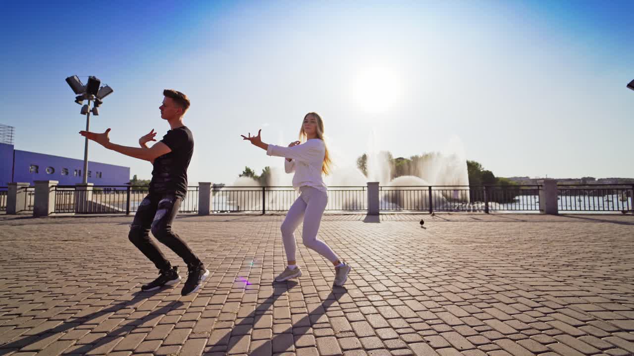Young couple dancing in the city. Active couple dancing hip hop choreography against the sunlight outdoors. Modern dance of teens on the fountain background.