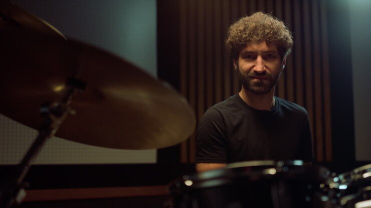 Batterista sorridente che suona al chiuso. Musicista allegro che guarda la telecamera in studio.