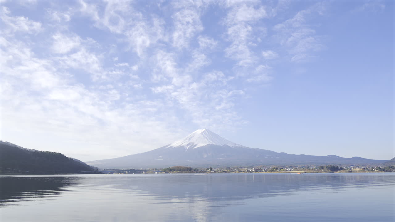 Spectacular view of Mount Fuji towering above Kawaguchiko Lake, with vibrant blue skies and fluffy white clouds creating a stunning backdrop during the day