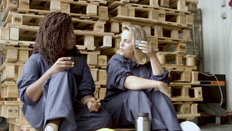 diverse workers talking, drinking coffee and eating cookies while sitting at wooden platform