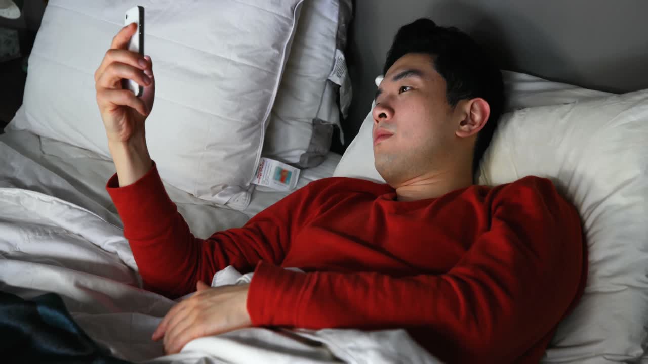 침대 4k에서 휴대폰을 사용하는 남자