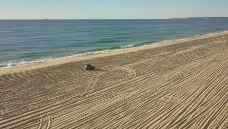 aerial view of a 4x4 car driving on empty beach near the sea, sideways tracking