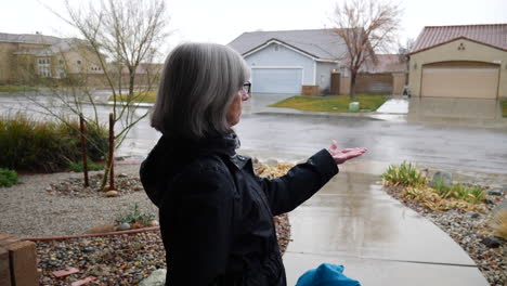 una mujer de mediana edad revisando el clima y sintiendo las gotas de lluvia de invierno con su mano en cámara lenta