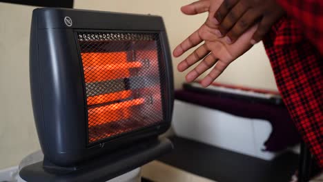 africano calentándose las manos en una habitación fría con un calentador