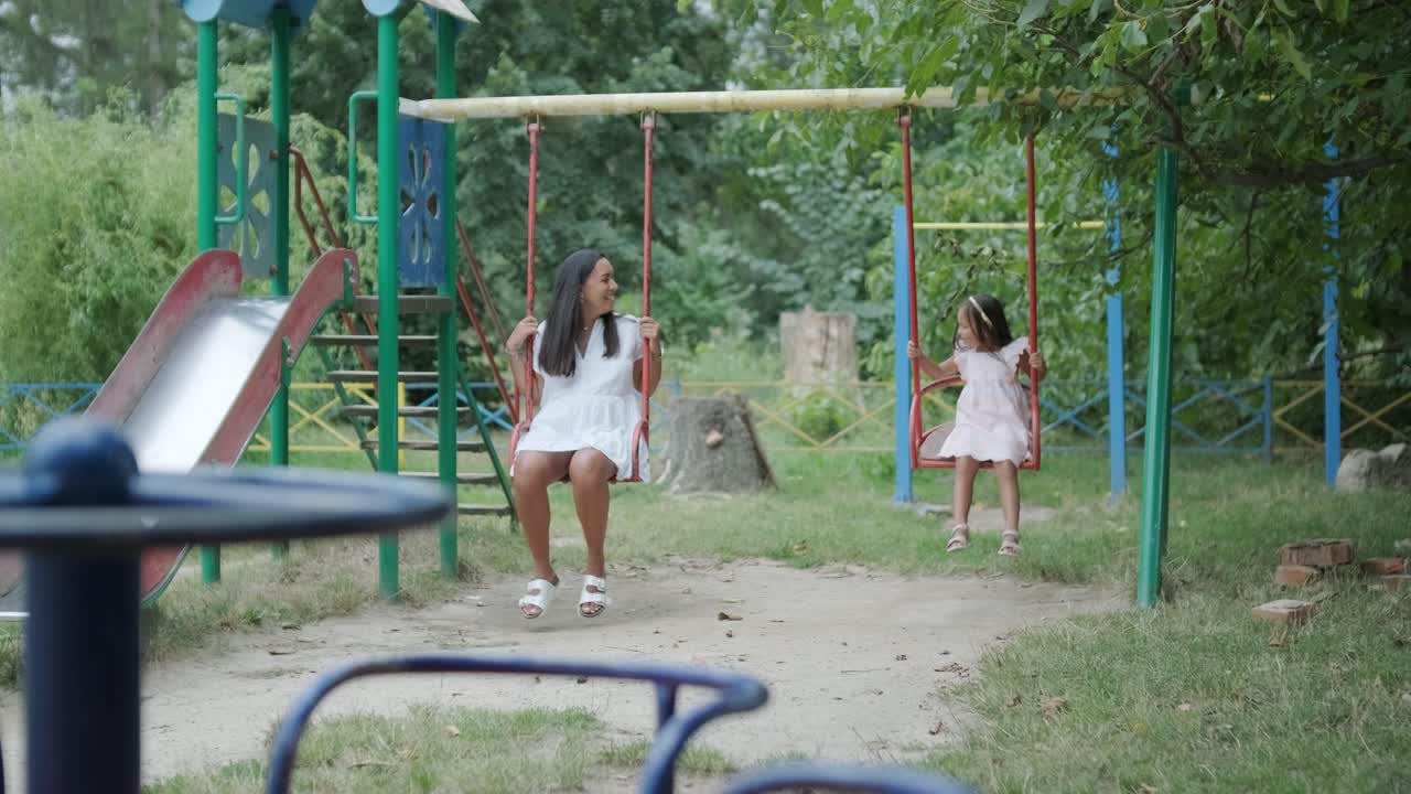 una madre embarazada y su hija joven disfrutan de un tiempo de juego juntos en un patio de recreo en el parque, rodeados de árboles y vegetación