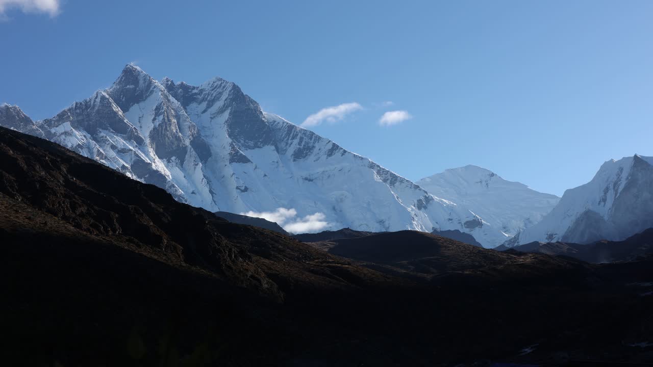 Majestic view of the Dhaulagiri Range in Nepal, showcasing towering snow-covered Himalayan peaks under a clear blue sky, dramatic light, and rugged terrain, evoking serenity and natural grandeur