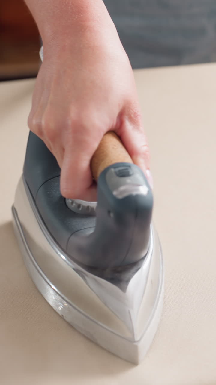 작업대 위 면에 재봉 다리미를 대고, 손으로 현대적인 밑판을 잡고 솔기를 다듬으며, 차분한 스튜디오에서 전문적인 기술로 옷감을 다듬고, 선명한 모서리와 옷감 텍스처를 강조한 의류