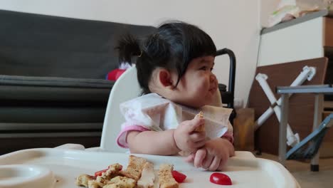 asian cute baby girl eating her homemade food on baby feeding chair