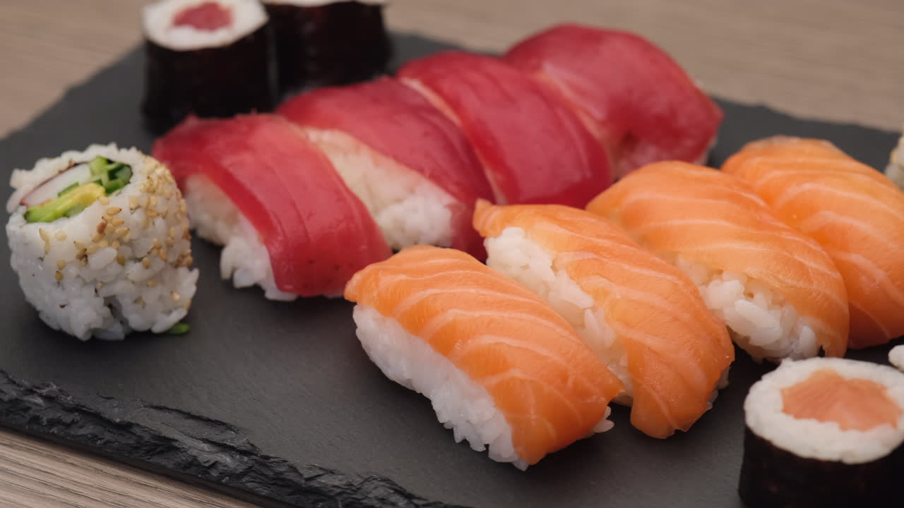 Sushi nigiri laks, nigiri tun, hosomaki og uramaki roterer på en tallerken
