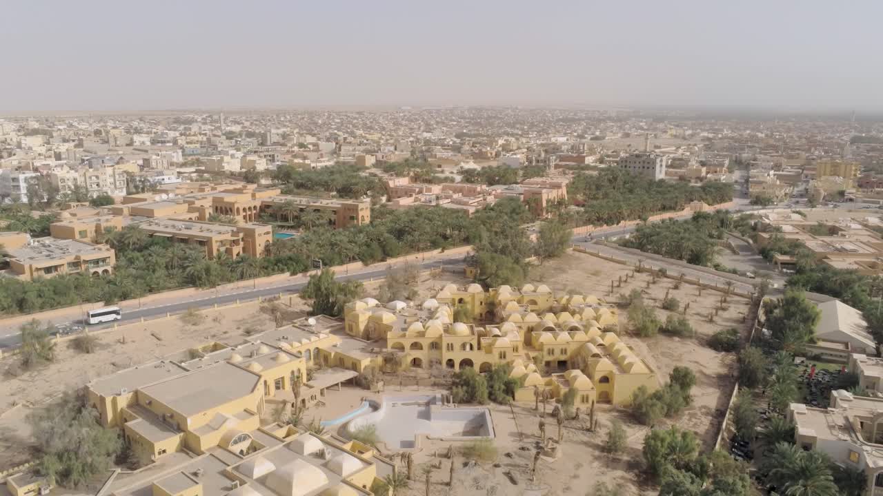 Drone footage capturing the contrast between the arid desert and lush palm-covered oasis