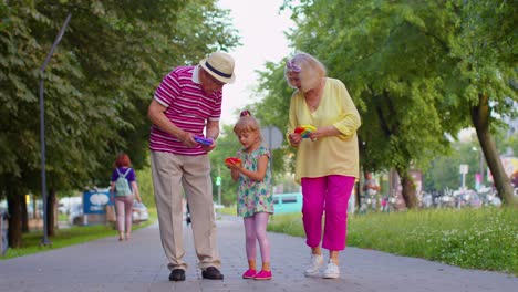 senior grandmother grandfather walking with granddaughter and playing anti-stress pop it toy game